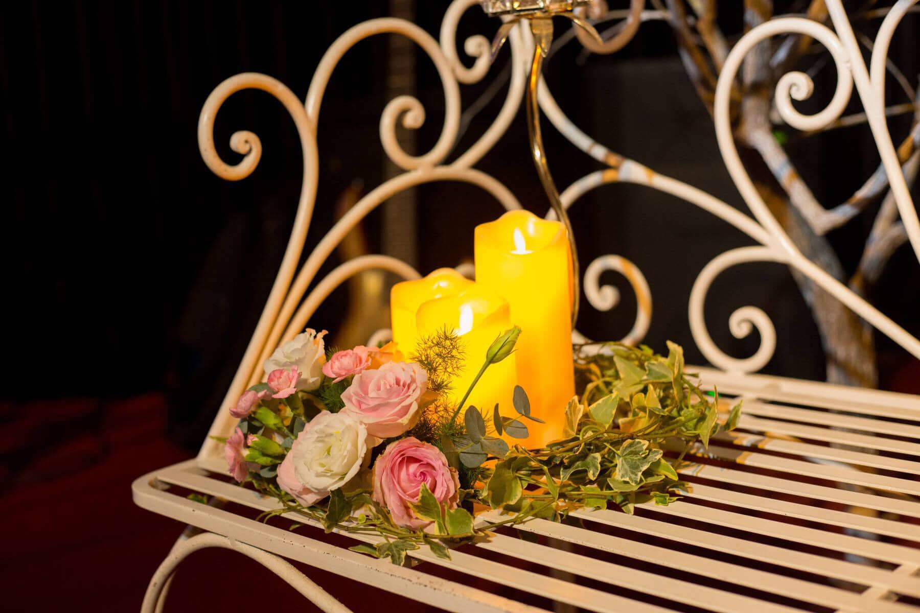 Nến v&agrave;ng v&agrave; hoa hồng tr&ecirc;n ghế kim loại trang tr&iacute;, tạo cảm gi&aacute;c ấm c&uacute;ng v&agrave; l&atilde;ng mạn.
