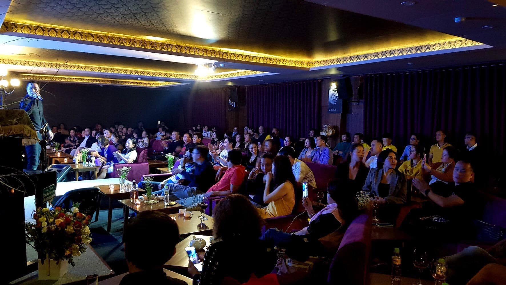 Kh&aacute;n giả ngồi trong một ph&ograve;ng k&iacute;n, &aacute;nh s&aacute;ng mờ, ch&uacute; &yacute; theo d&otilde;i sự kiện tr&ecirc;n s&acirc;n khấu.