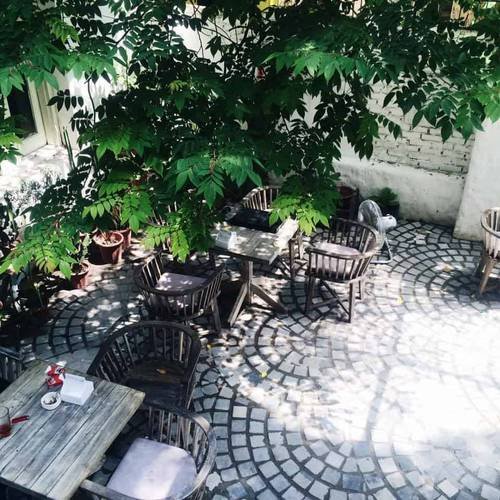 Khu vườn cà phê ngoài trời với bàn ghế gỗ và bóng cây xanh, tạo không gian thư giãn giữa thiên nhiên trong lành.