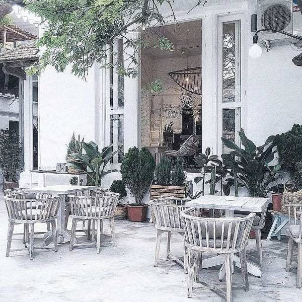 Qu&aacute;n c&agrave; ph&ecirc; ngo&agrave;i trời với b&agrave;n ghế gỗ, c&acirc;y xanh xung quanh, kh&ocirc;ng gian tho&aacute;ng đ&atilde;ng v&agrave; thiết kế hiện đại.