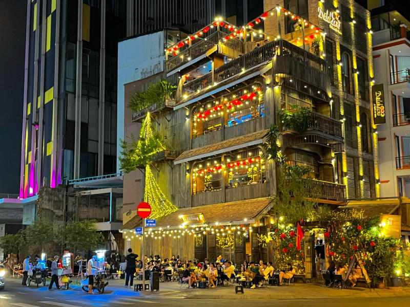 T&ograve;a nh&agrave; nhiều tầng với đ&egrave;n trang tr&iacute; s&aacute;ng rực, nhiều người ngồi b&ecirc;n ngo&agrave;i, khung cảnh nhộn nhịp v&agrave;o ban đ&ecirc;m.