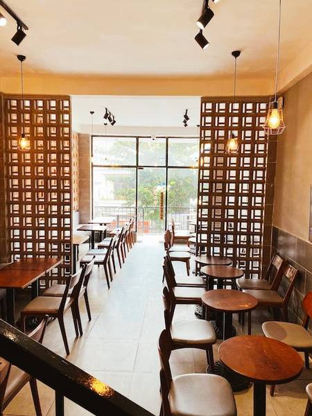 Qu&aacute;n c&agrave; ph&ecirc; với b&agrave;n ghế gỗ, &aacute;nh s&aacute;ng đ&egrave;n v&agrave;ng, cửa sổ lớn nh&igrave;n ra ngo&agrave;i trời, tạo kh&ocirc;ng gian ấm c&uacute;ng v&agrave; thoải m&aacute;i.