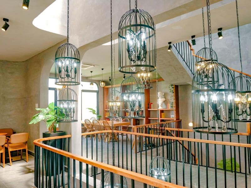 Kh&ocirc;ng gian nội thất với đ&egrave;n ch&ugrave;m trong lồng sắt, b&agrave;n ghế gỗ v&agrave; cầu thang, tạo cảm gi&aacute;c hiện đại v&agrave; tho&aacute;ng đ&atilde;ng.