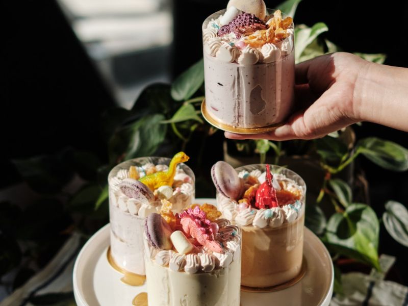 B&aacute;nh kem nhỏ trang tr&iacute; h&igrave;nh động vật v&agrave; macaron, đặt tr&ecirc;n b&agrave;n với c&acirc;y xanh l&agrave;m nền.