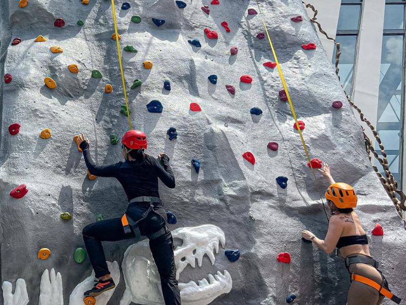 Hai người đang leo tường đ&aacute; nh&acirc;n tạo với mũ bảo hiểm v&agrave; d&acirc;y an to&agrave;n.