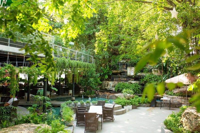 Khu vườn xanh m&aacute;t với nhiều c&acirc;y cối, b&agrave;n ghế ngo&agrave;i trời v&agrave; th&aacute;c nước nhỏ tạo kh&ocirc;ng gian thư gi&atilde;n.