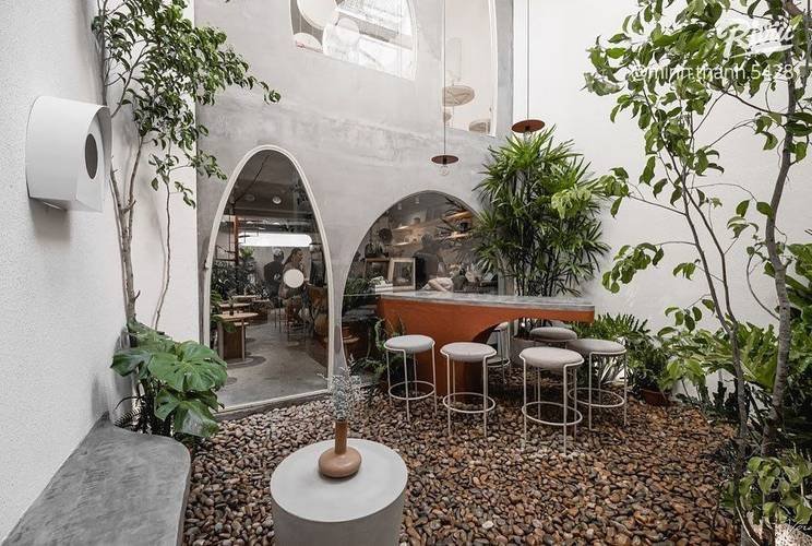 Không gian quán cafe ngoài trời, bàn ghế hiện đại, cây xanh xung quanh, ánh sáng tự nhiên, phong cách tối giản.