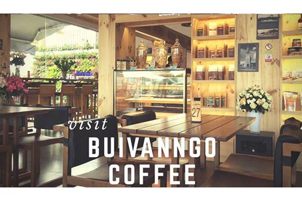 Quán cà phê với nội thất gỗ, tủ trưng bày, bàn ghế gỗ, hoa trang trí và ánh sáng ấm cúng.