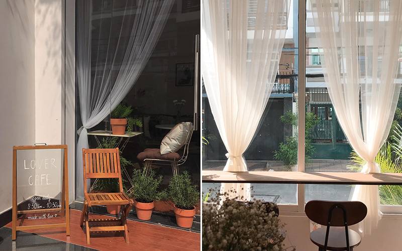 Hai g&oacute;c qu&aacute;n c&agrave; ph&ecirc; với ghế gỗ, r&egrave;m trắng v&agrave; c&acirc;y xanh, &aacute;nh s&aacute;ng tự nhi&ecirc;n chiếu qua cửa k&iacute;nh.