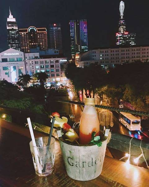 Đồ uống tr&ecirc;n b&agrave;n nh&igrave;n ra khu phố đ&ecirc;m với t&ograve;a nh&agrave; cao tầng v&agrave; xe cộ qua lại.