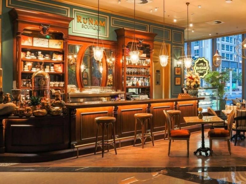 Qu&aacute;n c&agrave; ph&ecirc; sang trọng với quầy bar gỗ, đ&egrave;n treo trang tr&iacute;, b&agrave;n ghế cổ điển v&agrave; cửa sổ lớn nh&igrave;n ra ngo&agrave;i.