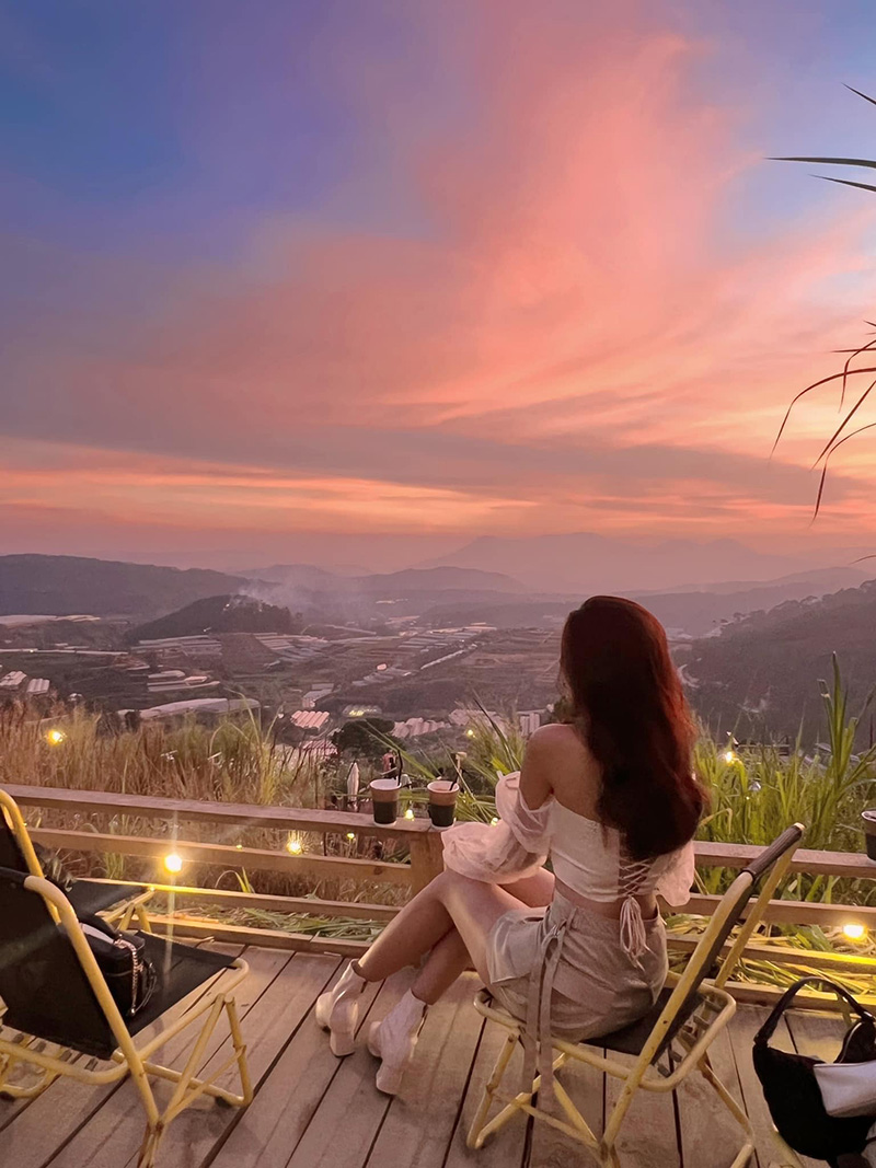 Người ngồi tr&ecirc;n ghế ngắm ho&agrave;ng h&ocirc;n ở qu&aacute;n c&agrave; ph&ecirc; ngo&agrave;i trời, ph&iacute;a trước l&agrave; thung lũng v&agrave; bầu trời đầy sắc m&agrave;u.