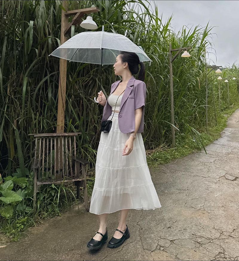 Người phụ nữ cầm &ocirc; trong suốt đứng tr&ecirc;n con đường nhỏ, b&ecirc;n cạnh l&agrave; ghế gỗ v&agrave; h&agrave;ng c&acirc;y xanh.