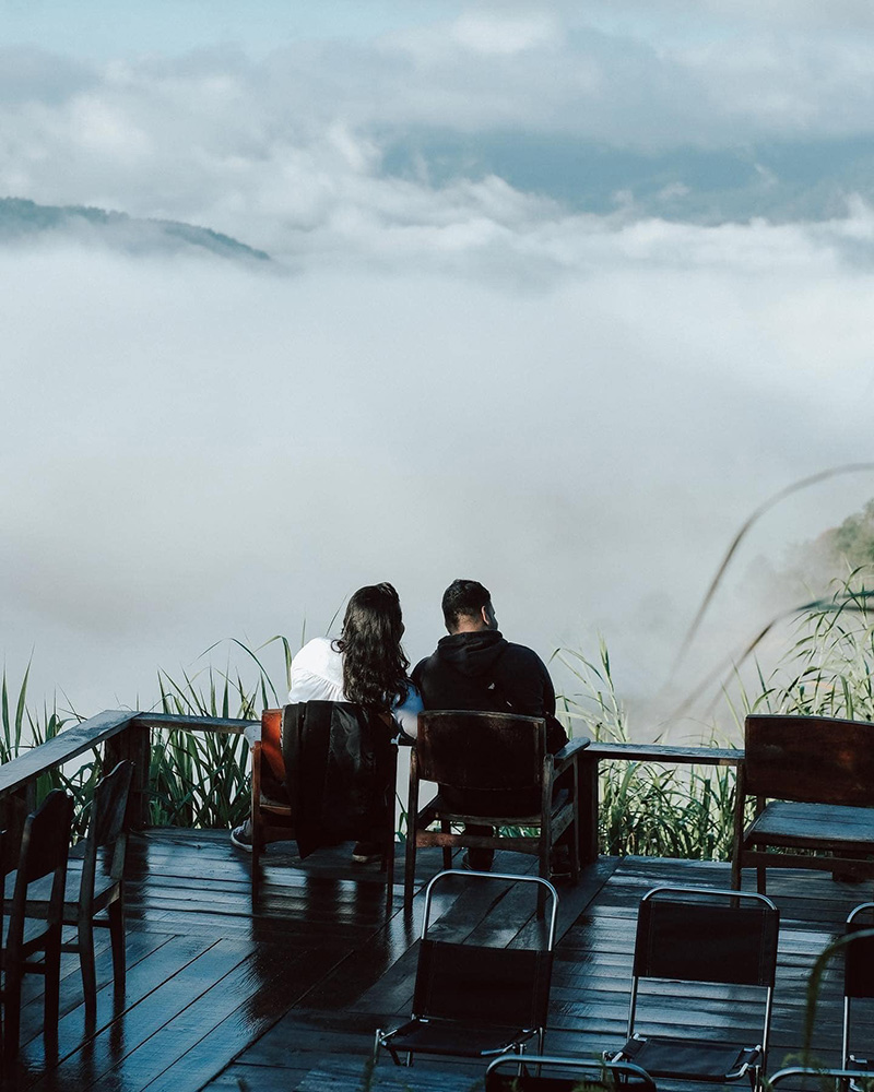 Hai người ngồi tr&ecirc;n s&acirc;n gỗ, nh&igrave;n ngắm biển m&acirc;y bao phủ khung cảnh n&uacute;i non ph&iacute;a trước.