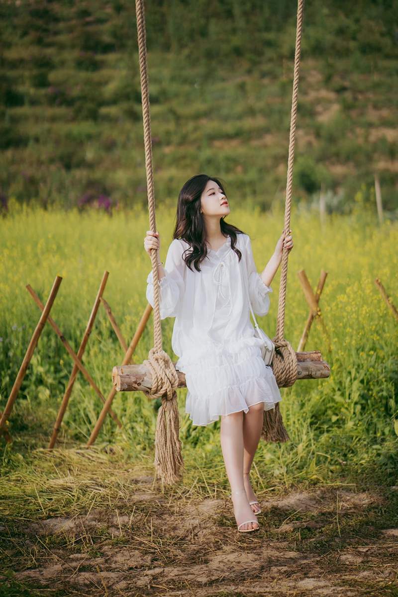 Người ngồi tr&ecirc;n x&iacute;ch đu bằng gỗ trong khung cảnh đồng cỏ xanh mướt, trời nắng nhẹ.