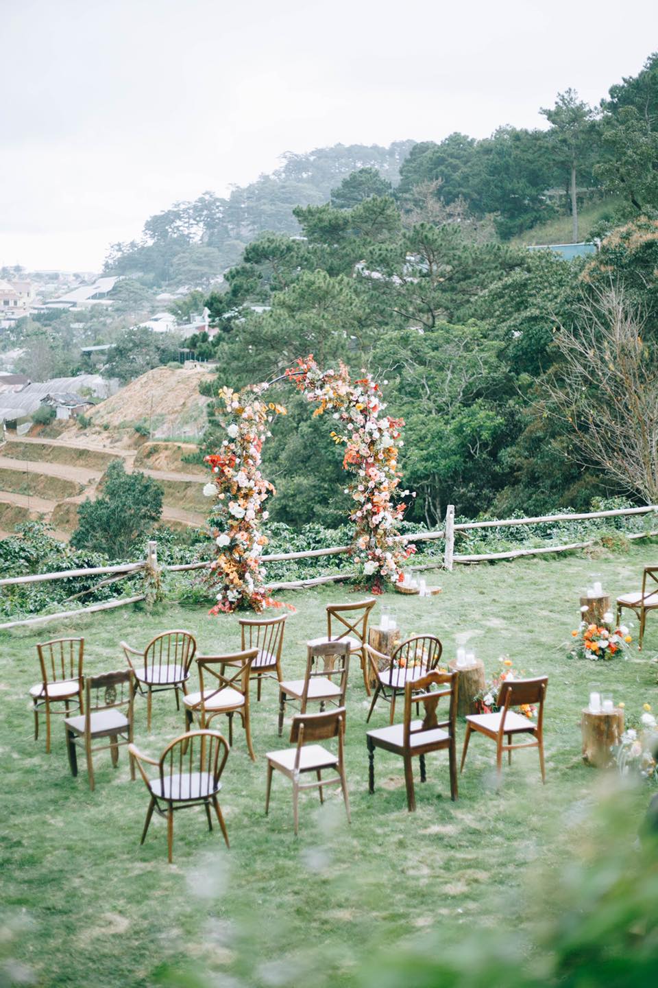 Khung cảnh ngo&agrave;i trời với ghế gỗ v&agrave; cổng hoa, nền l&agrave; c&acirc;y xanh v&agrave; n&uacute;i đồi.