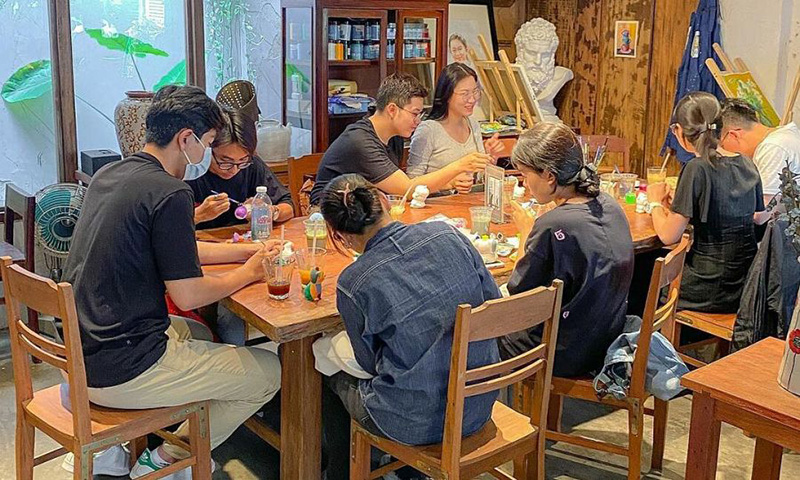 Nh&oacute;m người ngồi quanh b&agrave;n gỗ trong qu&aacute;n c&agrave; ph&ecirc;, c&ugrave;ng nhau vẽ v&agrave; tr&ograve; chuyện.