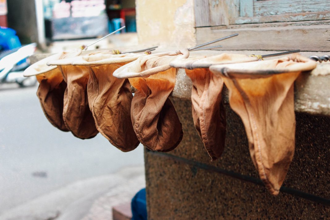 C&aacute;c t&uacute;i vải m&agrave;u n&acirc;u phơi tr&ecirc;n thanh kim loại, nền l&agrave; đường phố v&agrave; t&ograve;a nh&agrave;.