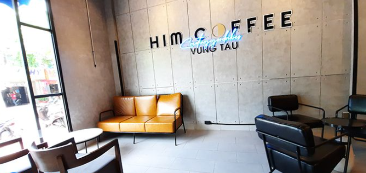 Quán cà phê hiện đại với ghế sofa vàng, bàn ghế đen, tường ghi xám có chữ trang trí.