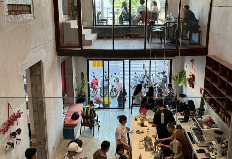 Qu&aacute;n c&agrave; ph&ecirc; đ&ocirc;ng kh&aacute;ch với kh&ocirc;ng gian hai tầng, nhiều người đang l&agrave;m việc v&agrave; tr&ograve; chuyện.