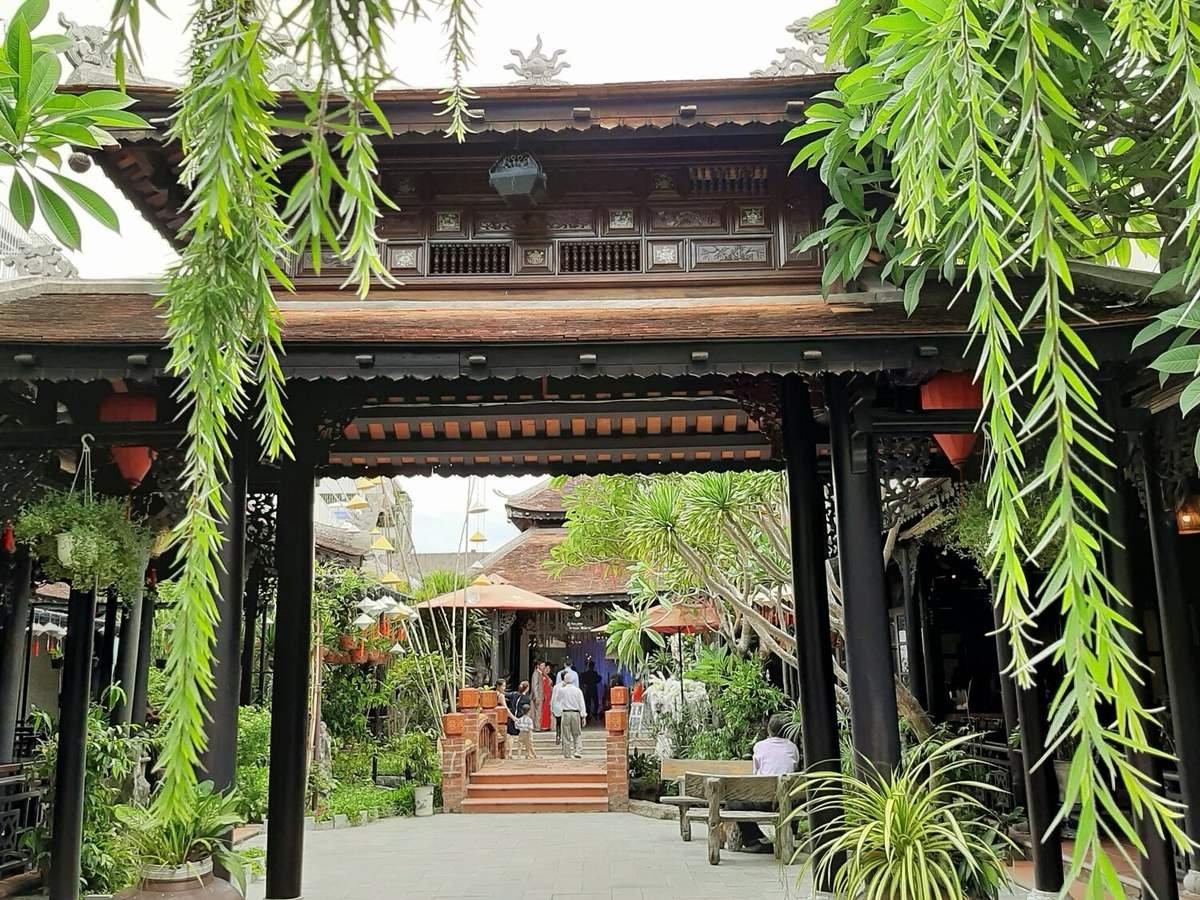 Cổng vào nhà cổ Việt Nam với mái ngói, cây xanh, nội thất gỗ truyền thống trong khung cảnh thanh bình.