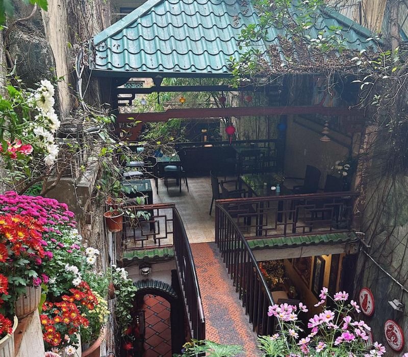 Một góc quán cafe ngoài trời với hoa tươi và quang cảnh thiên nhiên, tạo không gian thư giãn.