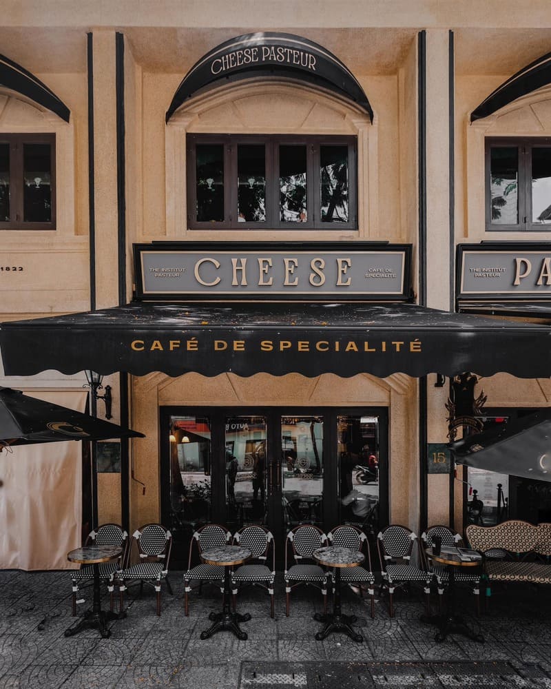 Mặt tiền qu&aacute;n c&agrave; ph&ecirc; với bảng hiệu "Caf&eacute; de Specialit&eacute;" v&agrave; d&atilde;y b&agrave;n ghế ngo&agrave;i trời kh&ocirc;ng c&oacute; người ngồi.