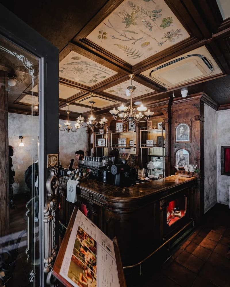 Qu&aacute;n c&agrave; ph&ecirc; phong c&aacute;ch cổ điển với quầy gỗ v&agrave; trần họa tiết, đ&egrave;n ch&ugrave;m trang tr&iacute; sang trọng.