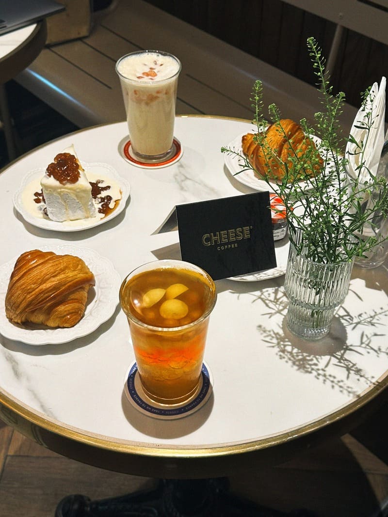 B&agrave;n tr&ograve;n với b&aacute;nh ngọt, nước uống v&agrave; c&acirc;y xanh nhỏ, tr&ecirc;n mặt b&agrave;n trắng.