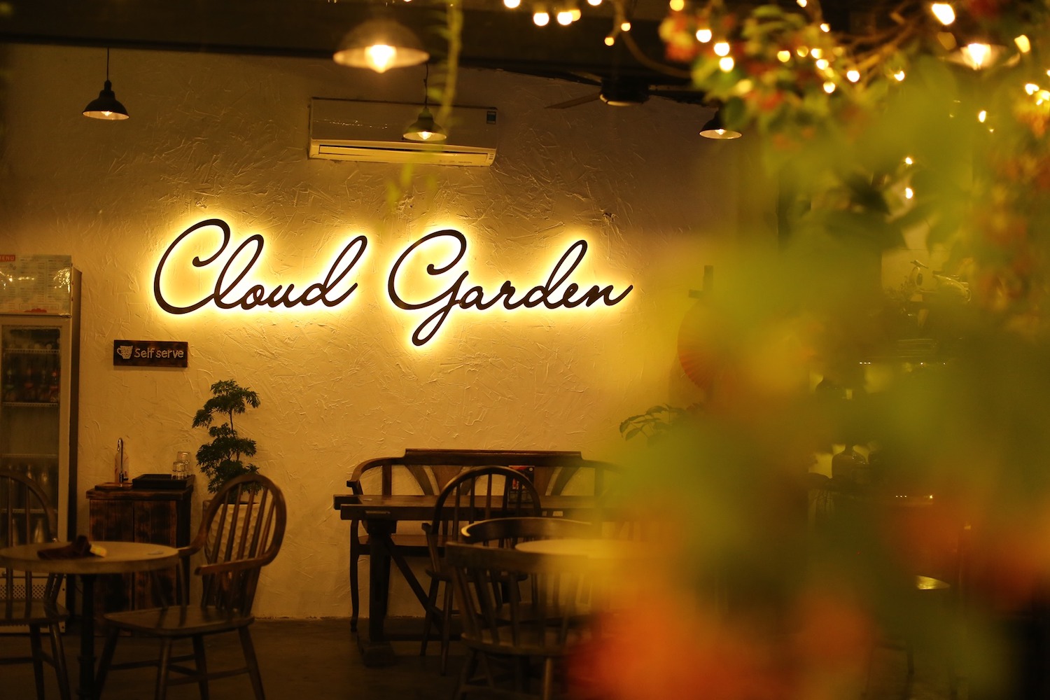 Kh&ocirc;ng gian qu&aacute;n c&agrave; ph&ecirc; ấm c&uacute;ng với bảng hiệu "Cloud Garden" s&aacute;ng đ&egrave;n v&agrave; b&agrave;n ghế gỗ xung quanh.