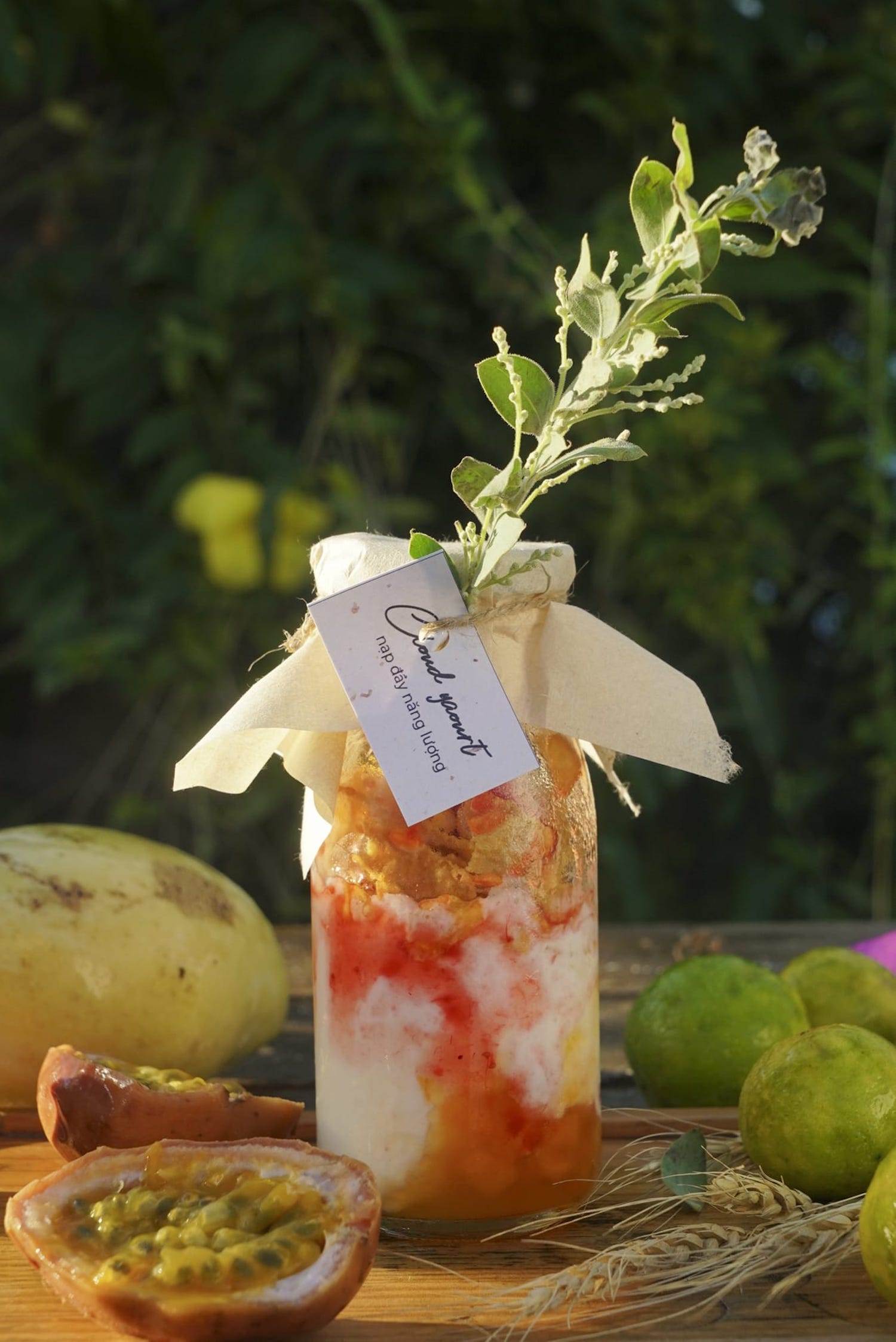 Lọ thủy tinh chứa thức uống m&agrave;u sắc, trang tr&iacute; với l&aacute; c&acirc;y, b&ecirc;n cạnh l&agrave; c&aacute;c loại tr&aacute;i c&acirc;y tr&ecirc;n b&agrave;n gỗ.