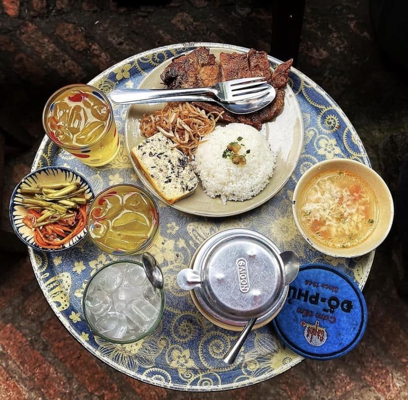 Khám Phá Cà Phê Đỗ Phủ: Sự Giao Thoa Giữa Ẩm Thực và Lịch Sử 2 Bữa cơm Việt Nam với thịt nướng, đậu phụ, cơm trắng, canh trứng, đồ chua, và trà đá trên bàn trang trí hoa văn.