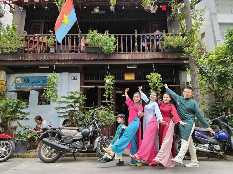 com-tam-do-phu-2-1744593345 Một nhóm người mặc áo dài đứng tạo dáng trước ngôi nhà cổ, có xe máy và cờ Việt Nam.