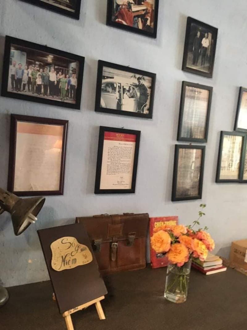 com-tam-do-phu-3-1744593345 Các khung ảnh treo trên tường, bên dưới là bàn có lọ hoa, sách, và một bảng đứng nhỏ.