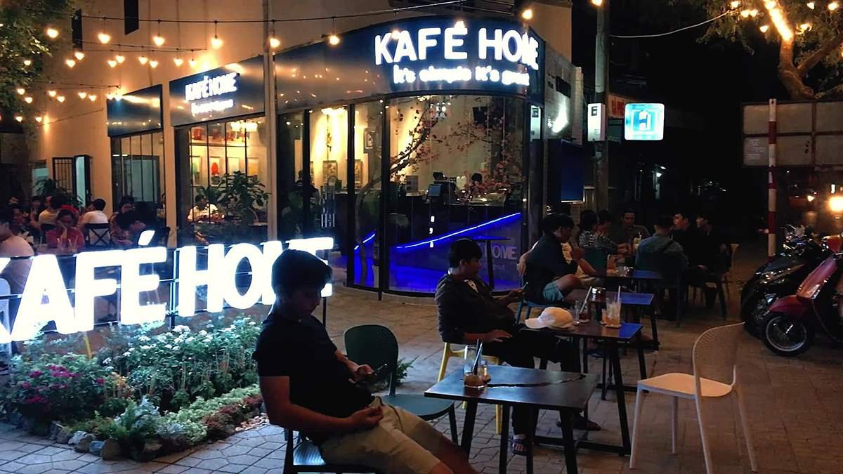 Quán cà phê đêm với ánh đèn ấm áp, khách hàng ngồi ngoài trời thư giãn, bảng hiệu Kafé Home.