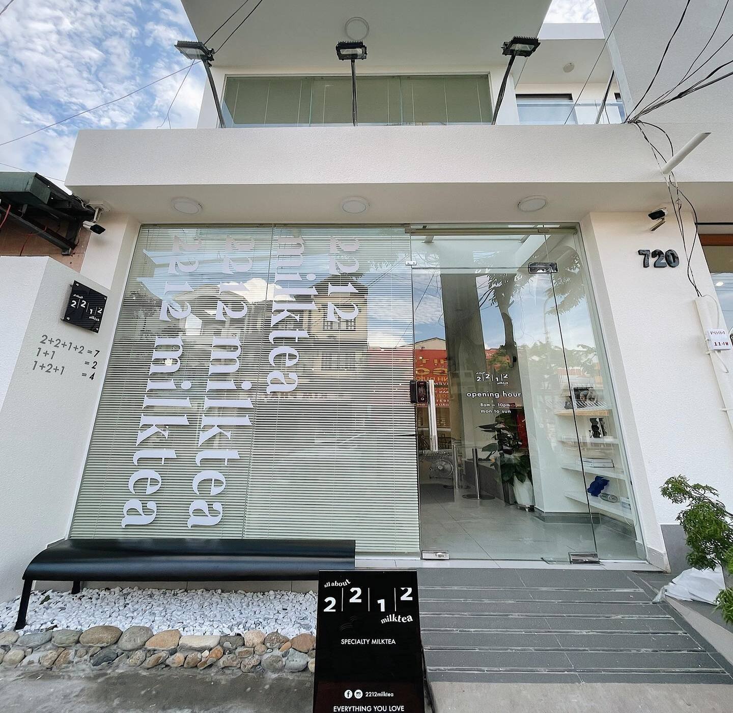 Mặt tiền cửa h&agrave;ng tr&agrave; sữa với cửa k&iacute;nh, biển hiệu v&agrave; ghế ngồi b&ecirc;n ngo&agrave;i. Số địa chỉ hiện r&otilde; tr&ecirc;n tường.