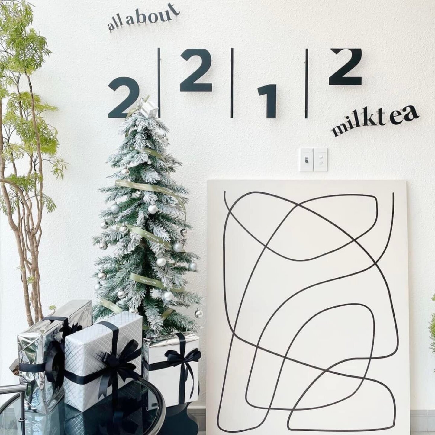 C&acirc;y th&ocirc;ng trang tr&iacute;, tranh trừu tượng v&agrave; qu&agrave; tặng b&ecirc;n cạnh d&ograve;ng chữ tr&ecirc;n tường trắng.