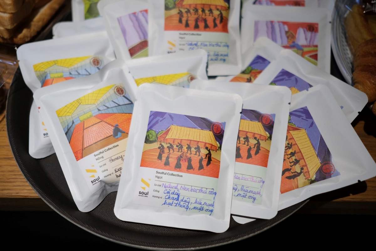 G&oacute;i c&agrave; ph&ecirc; với nh&atilde;n m&agrave;u sắc sặc sỡ, đặt tr&ecirc;n khay đen, c&oacute; h&igrave;nh minh họa người m&uacute;a v&agrave; cảnh quan.