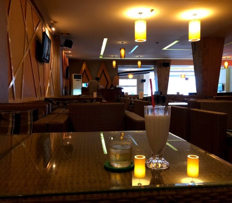 Quán cà phê ấm cúng với ánh sáng vàng, kính nước và ly sinh tố trên bàn.