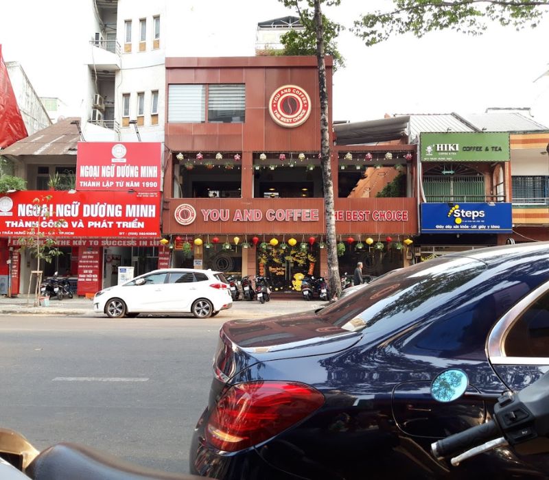 H&agrave;ng qu&aacute;n c&agrave; ph&ecirc; v&agrave; trung t&acirc;m ngoại ngữ tr&ecirc;n đường phố, c&oacute; xe hơi v&agrave; xe m&aacute;y đậu ph&iacute;a trước.