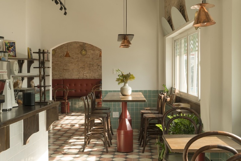 Qu&aacute;n c&agrave; ph&ecirc; với b&agrave;n ghế gỗ, &aacute;nh s&aacute;ng tự nhi&ecirc;n qua cửa sổ, trang tr&iacute; đơn giản v&agrave; c&acirc;y xanh.