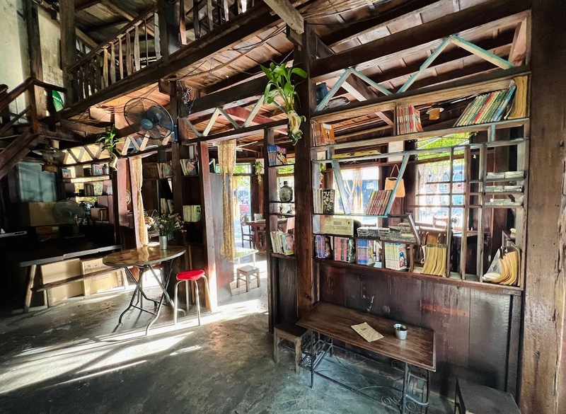 Kh&ocirc;ng gian nội thất gỗ của qu&aacute;n c&agrave; ph&ecirc; với kệ s&aacute;ch, b&agrave;n nhỏ v&agrave; &aacute;nh s&aacute;ng tự nhi&ecirc;n chiếu qua cửa sổ.