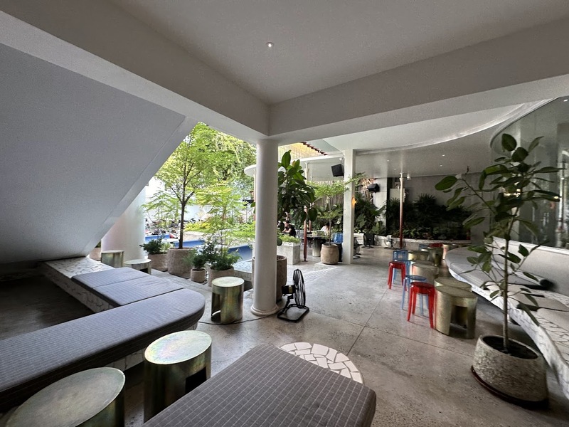 Kh&ocirc;ng gian qu&aacute;n c&agrave; ph&ecirc; rộng r&atilde;i với ghế nệm, b&agrave;n nhỏ, c&acirc;y xanh v&agrave; &aacute;nh s&aacute;ng tự nhi&ecirc;n từ cửa sổ lớn.