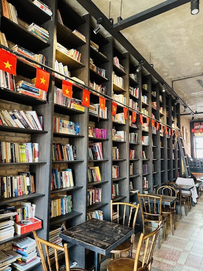 Kệ s&aacute;ch cao với nhiều s&aacute;ch, b&agrave;n ghế gỗ ph&iacute;a trước, trang tr&iacute; cờ nhỏ m&agrave;u đỏ c&oacute; sao v&agrave;ng.