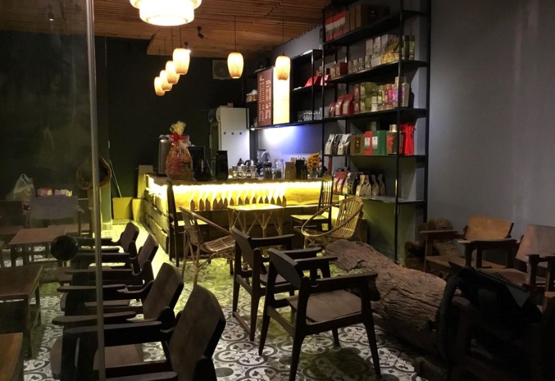 Qu&aacute;n c&agrave; ph&ecirc; với &aacute;nh s&aacute;ng ấm &aacute;p, b&agrave;n ghế gỗ v&agrave; kệ trưng b&agrave;y c&aacute;c sản phẩm.