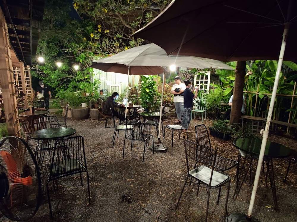 Qu&aacute;n c&agrave; ph&ecirc; ngo&agrave;i trời v&agrave;o buổi tối với nhiều b&agrave;n ghế v&agrave; kh&aacute;ch h&agrave;ng đang tr&ograve; chuyện dưới &aacute;nh đ&egrave;n.