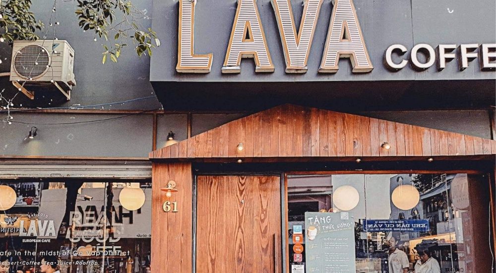 Khám Phá 10 Quán Cafe Gò Vấp Với Góc "Hidden Gem" Độc Đáo 15 Mặt tiền quán cà phê với biển hiệu lớn, cửa gỗ và bảng thông tin chương trình khuyến mãi dán bên ngoài.