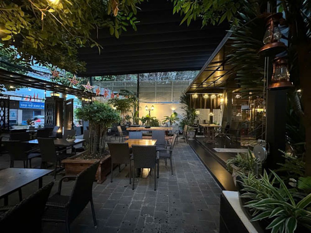 Khám Phá Top 10 Quán Cafe Sân Vườn Đẹp và Thư Giãn Tại Thủ Đức 11 Quán cà phê ngoài trời vào buổi tối, có bàn ghế sắp xếp gọn gàng, cây xanh và đèn trang trí.