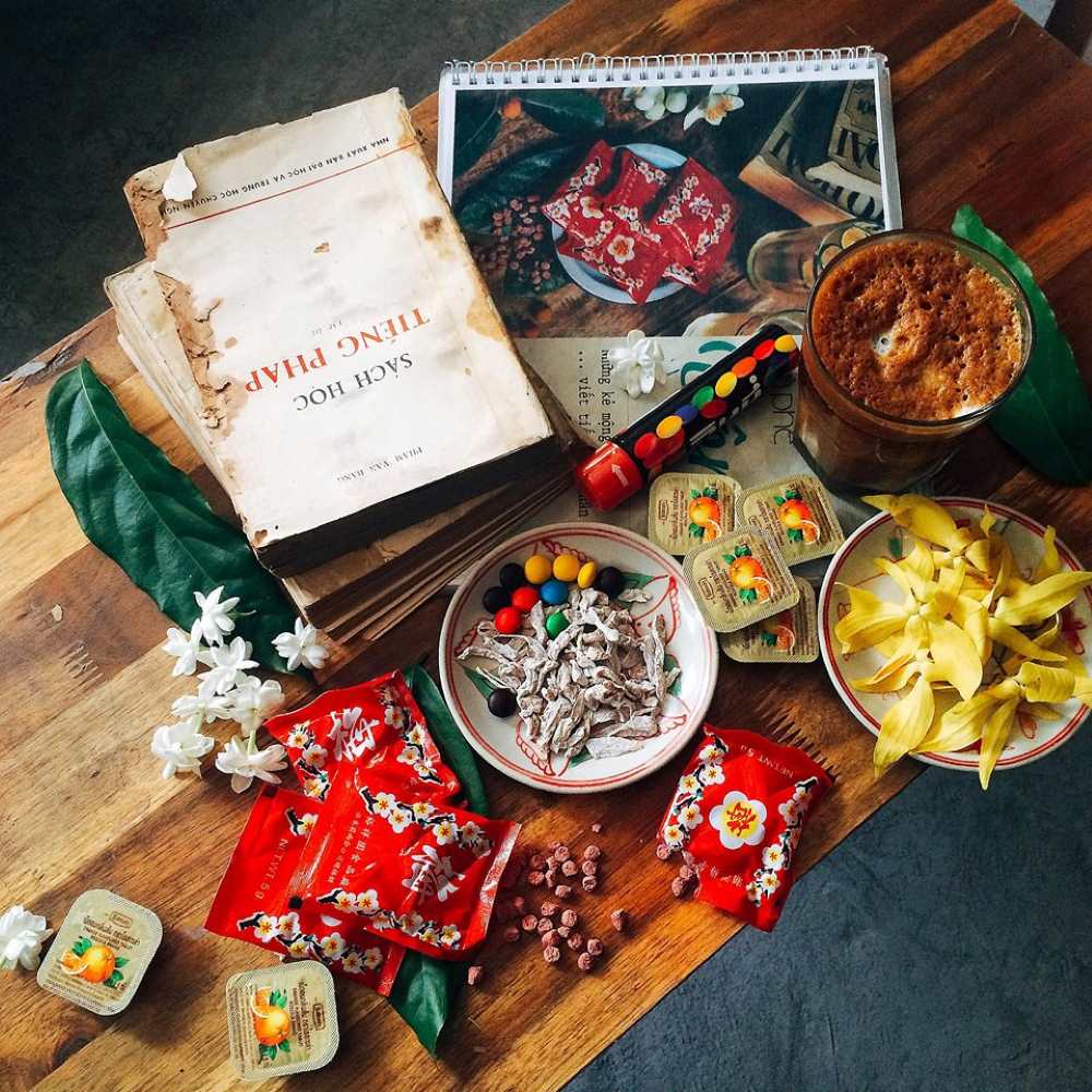 Khám Phá 10+ Quán Cafe Đẹp Nhất Long Biên: Thỏa Sức “Sống Ảo”, Thưởng Thức Đồ Uống Ngon 12 Sách, hoa và đồ ăn vặt trên bàn gỗ, bao gồm kẹo, trái cây sấy khô và đồ uống trong ly thủy tinh.