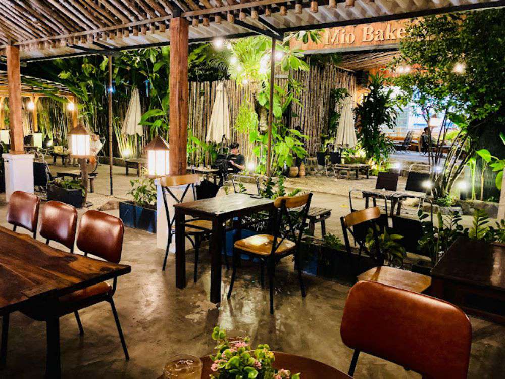 Khám Phá Top 10 Quán Cafe Sân Vườn Đẹp và Thư Giãn Tại Thủ Đức 8 Quán cà phê ngoài trời với bàn ghế gỗ, cây xanh xung quanh và ánh đèn tạo không gian ấm cúng.